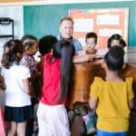 Nauczycielka przy pianinie prowadzi grupę dzieci na lekcji muzyki